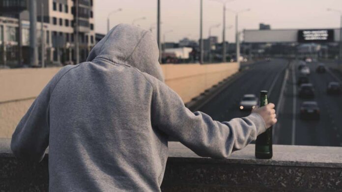 chico con botella en la mano mirando a un puente donde pasan coches