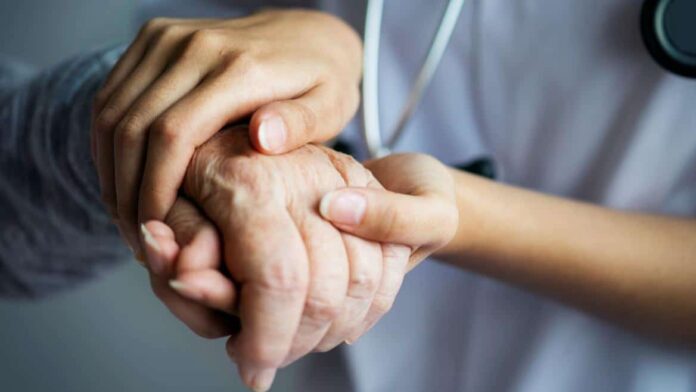 Un sanitario coge las manos de una persona mayor