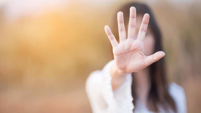 Mujer con el brazo estirado y la palma de la mano abierta tapando su cara