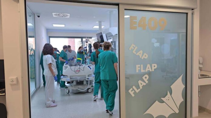 profesionales con pijama verde al fondo pasillo tras puerta con una cama de hospital