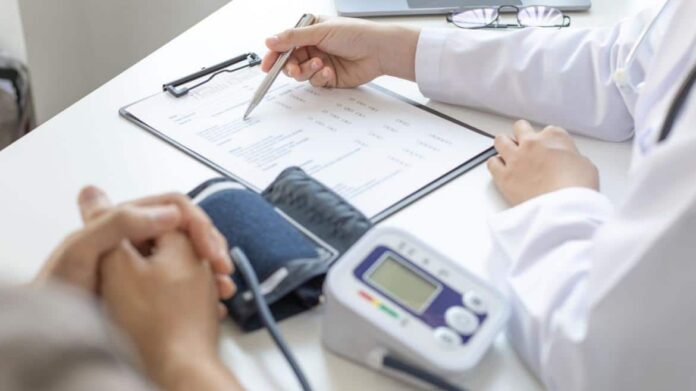 foto de mano de médico escribiendo en formulario con t4ensiómetro al lado y manos de paciente