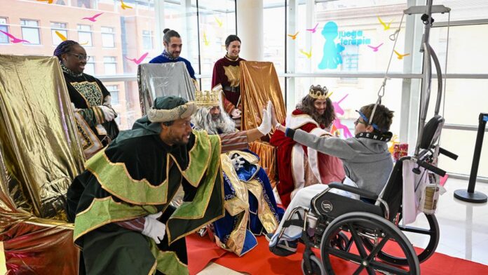 Un niño en silla de ruedas choca la mano con los Reyes Magos
