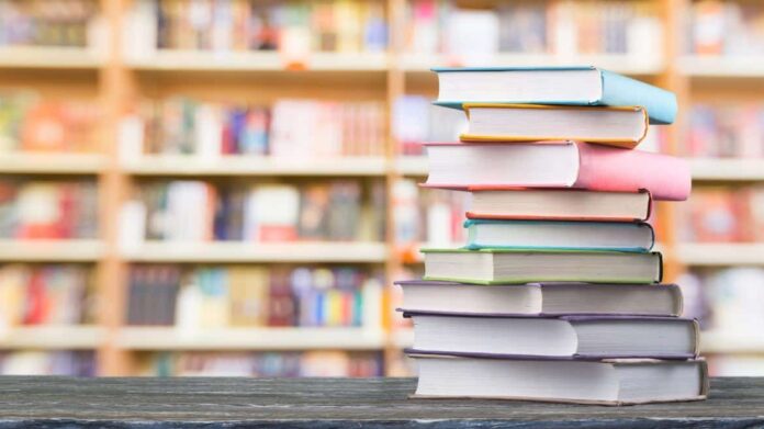Libros forrados de colores apilados y fondo de gran libreria con numerosos estantes