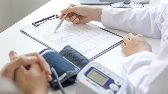 médico escribiendo en formulario con tensiómetro al lado y manos de paciente