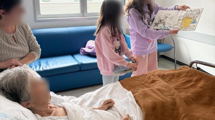 Niñas leen a paciente en cama