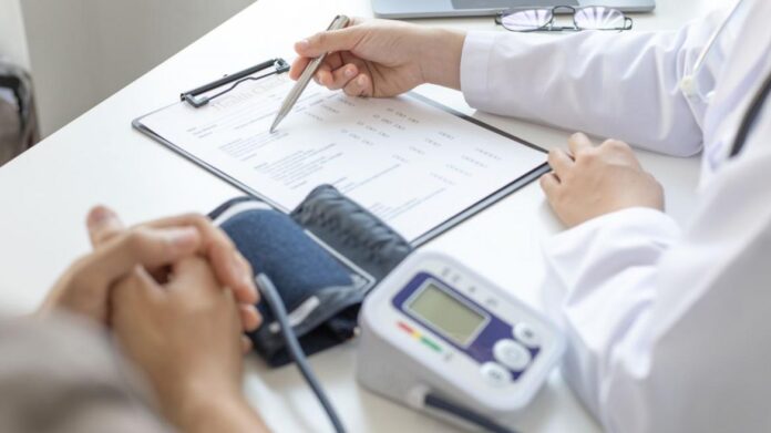 médico escribiendo en formulario con tensiómetro al lado y manos de paciente