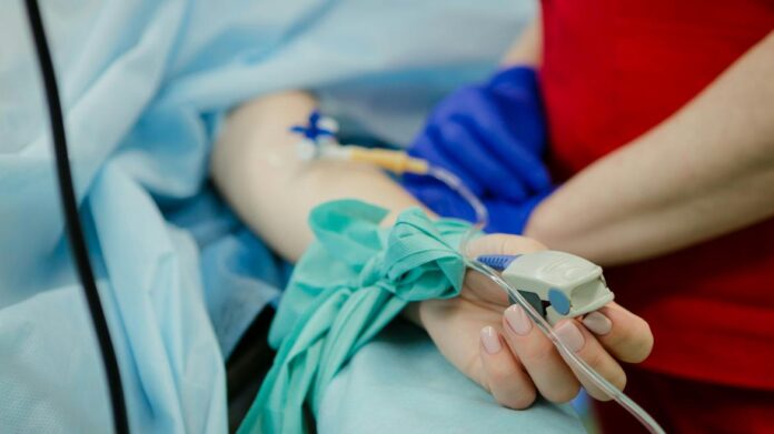 Paciente en una cama con un pulsioxímetro en el dedo, atendido por un profesional sanitario 