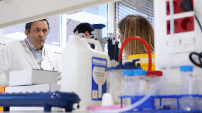 Un hombre con bata blanca en un laboratorio al fondo en primer plano material.