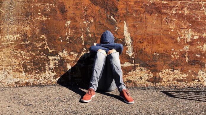 Joven triste sentado en el suelo en la calle
