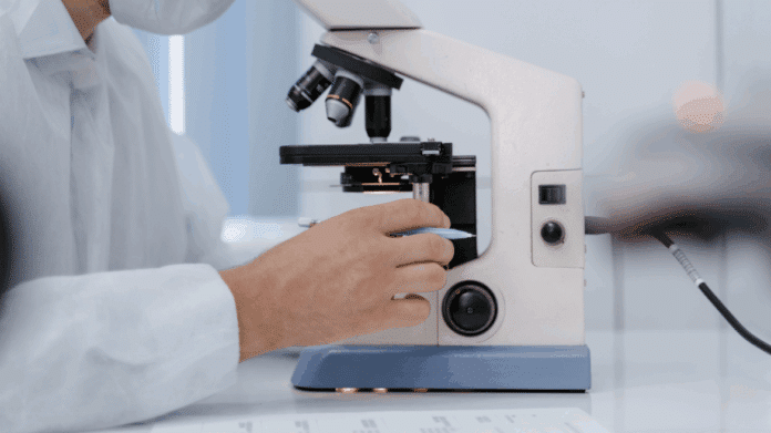 Mano de hombre con bata blanca sobre un microscopio que ocupa casi toda la imagen