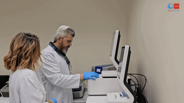 Dos investigadores hombre y mujer en un laboratorio frente a unas máquinas en un plano de perfil