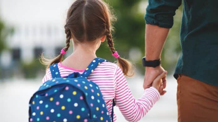 The Community of Madrid increases aid by 40% for A girl with her back turned, held by the hand of an adult.