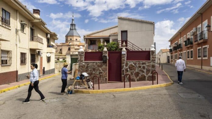 La Comunidad de Madrid Anunciará Inversión de 284 Millones para Calles de Loeches, al fondo la iglesia, en primer plano una persona pintando un cuadro apoyado en un caballete sobre la acera